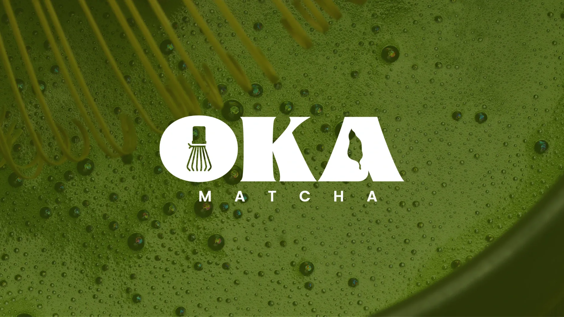 Le logotype Oka Matcha en blanc sur un bol de matcha fouetté, la mousse verte couverte de bulles et les brins du fouet en haut à gauche
