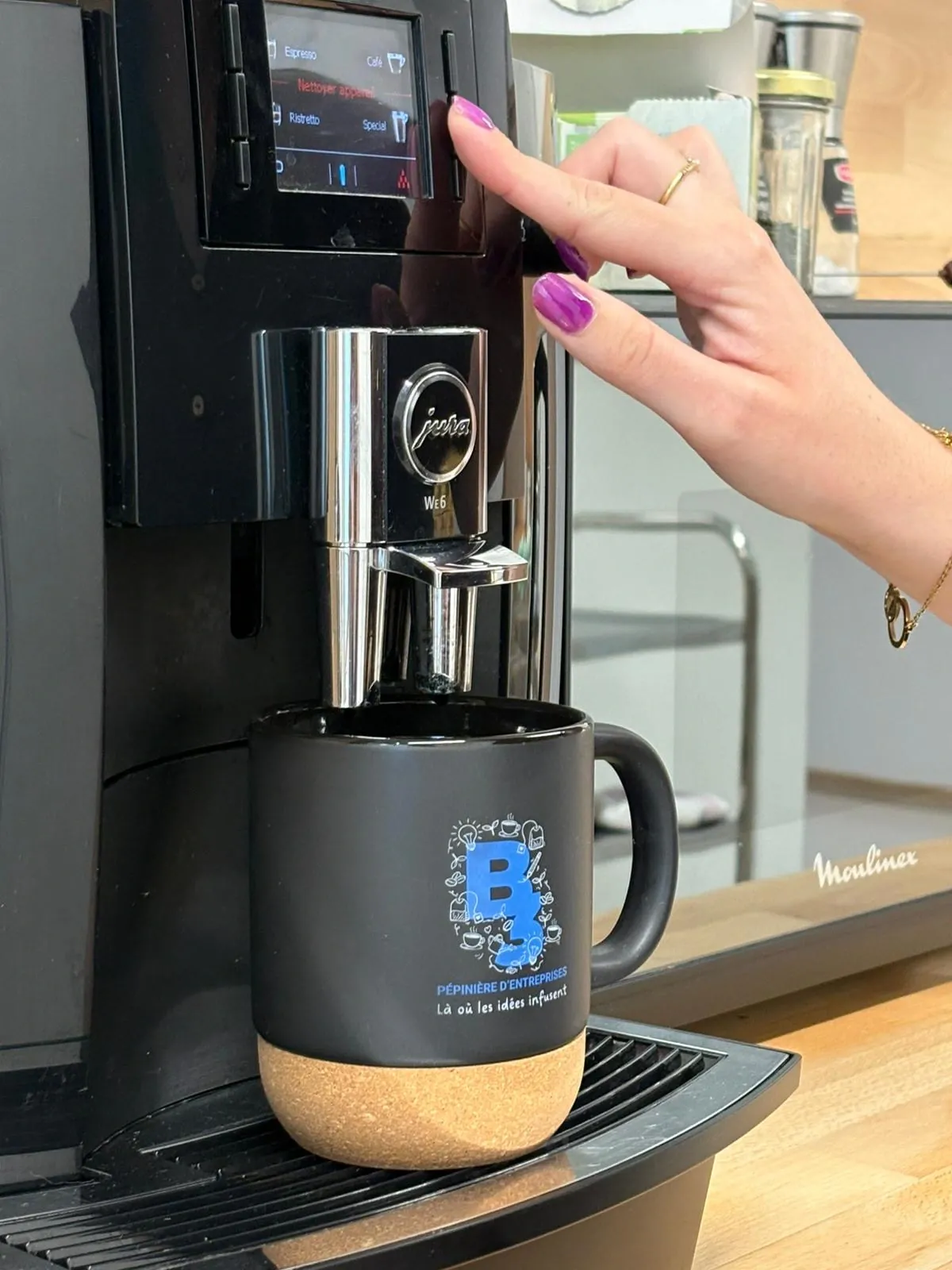 La tasse placée sous la machine à café, une main appuyant sur le bouton de l’appareil